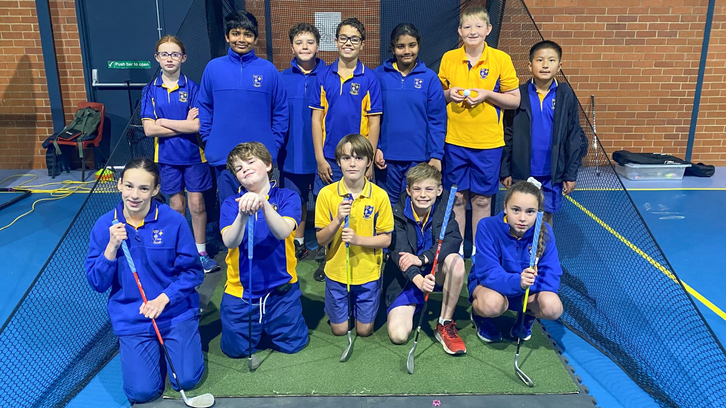 A group of kids in front of the net posing with golf clubvs