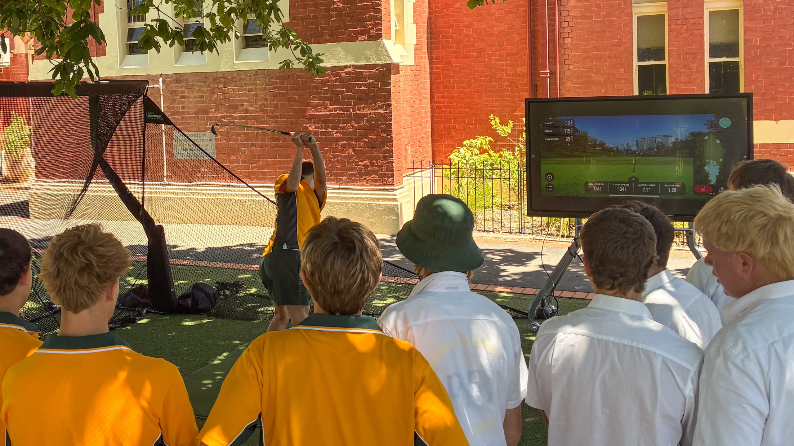 Kids watch on as a boy hits a golf ball into a net